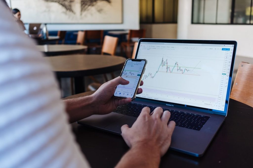 A man using trading charts on his smartphone and laptop